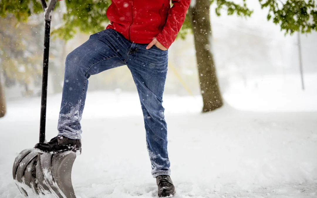 Closeup shot fo a male with his foot on the snow shovel while standing in a snowy field